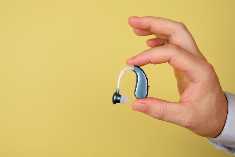 A behind-the-ear hearing aid held in hand, symbolizing tinnitus relief through better hearing.