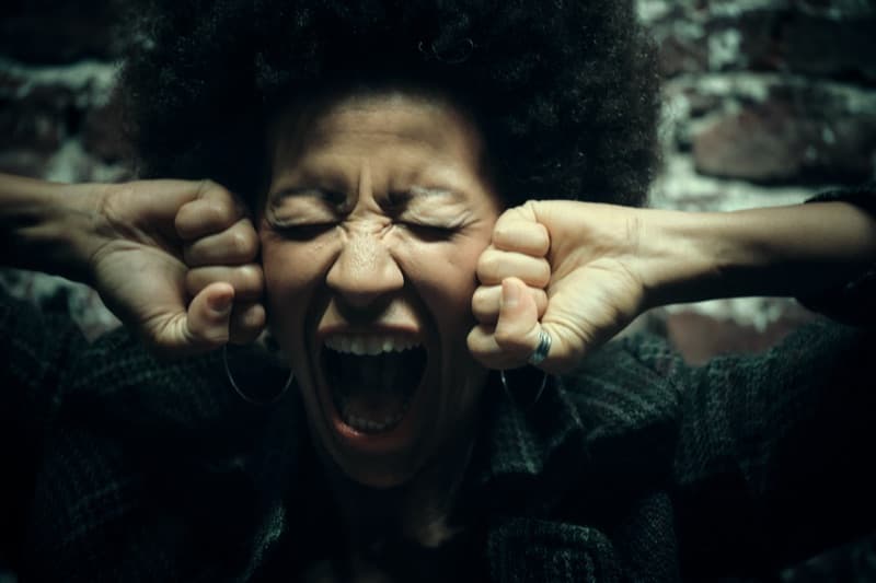 Woman pressing her fists against her ears and crying out, conveying how painfully loud ordinary sound can feel with hyperacusis.