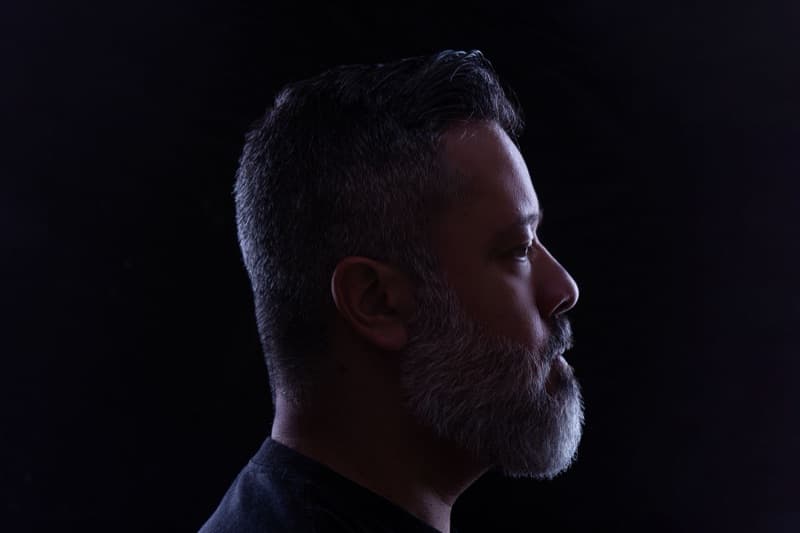Side profile of a man in low light with his ear turned toward the viewer, reflecting the sudden one-sided hearing change that often brings on tinnitus.
