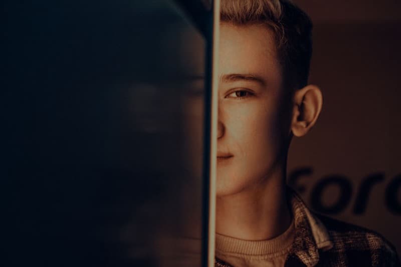 A young man lit from one side, with half his face and one ear visible against deep shadow.
