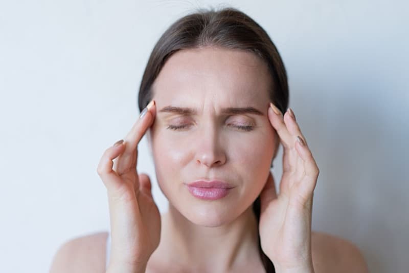 Woman with her eyes closed pressing her fingertips to both temples during a sudden tinnitus spike.