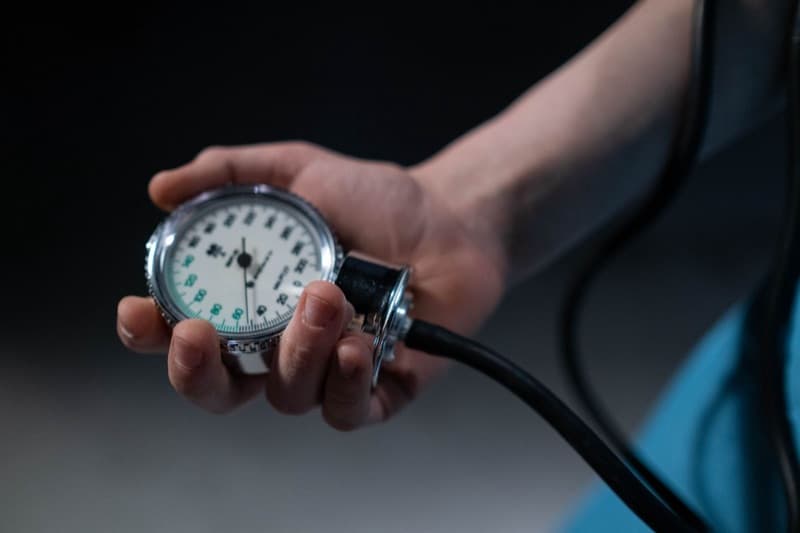Close-up of a clinician's hand holding a blood pressure gauge against a dark background.