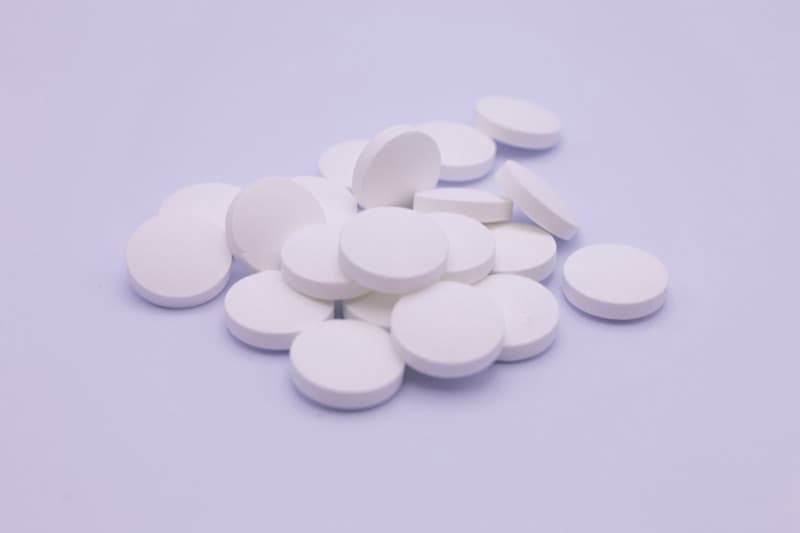 A small pile of round white magnesium tablets on a pale lilac surface.