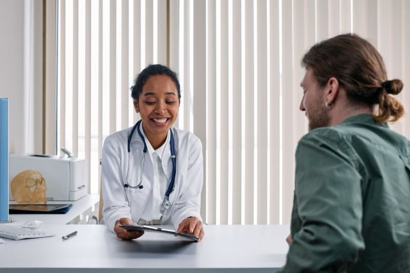 A smiling doctor talking with a patient across a desk during a consultation about hearing and tinnitus symptoms.