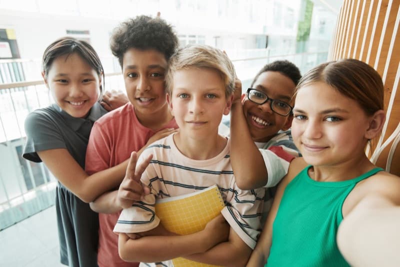 A group of smiling schoolchildren standing together in a bright school hallway.